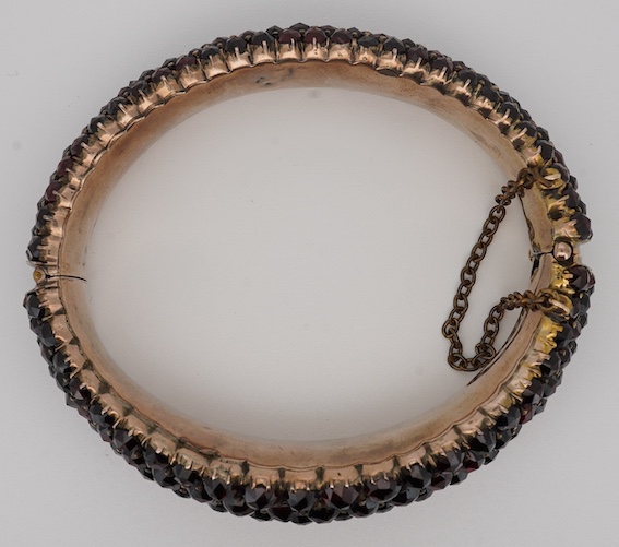 An Edwardian yellow metal overlaid and facetted garnet cluster set hinged bracelet, with safety chain, interior diameter 59mm. Condition - poor to fair